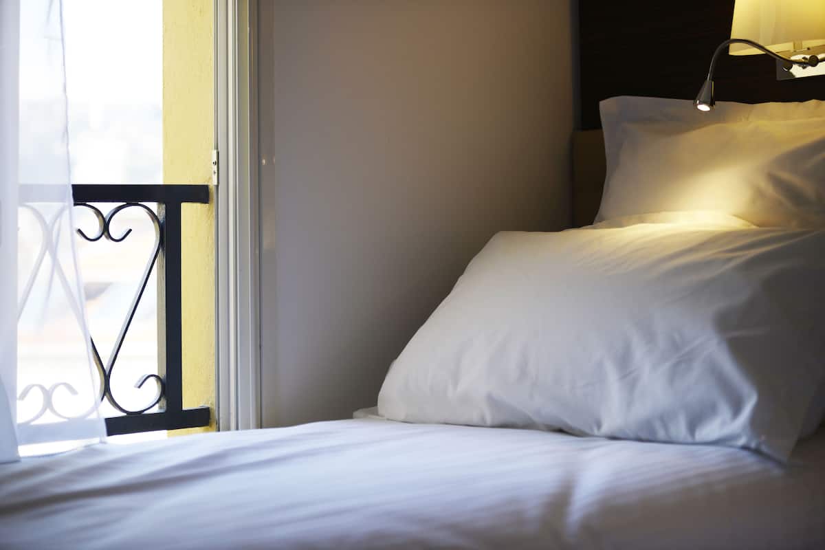 A hotel room with a bed, a window with a view, and a nightstand with a lamp.