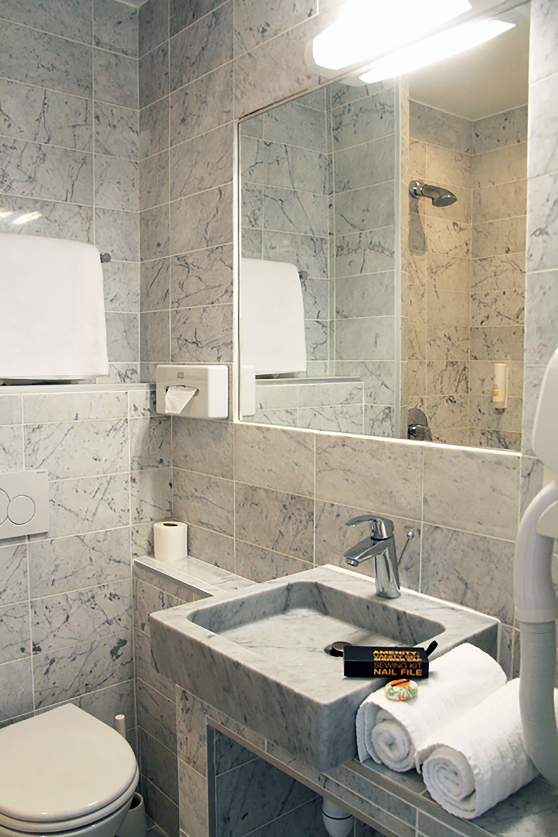 A bathroom with a marble sink, a toilet, and a mirror.