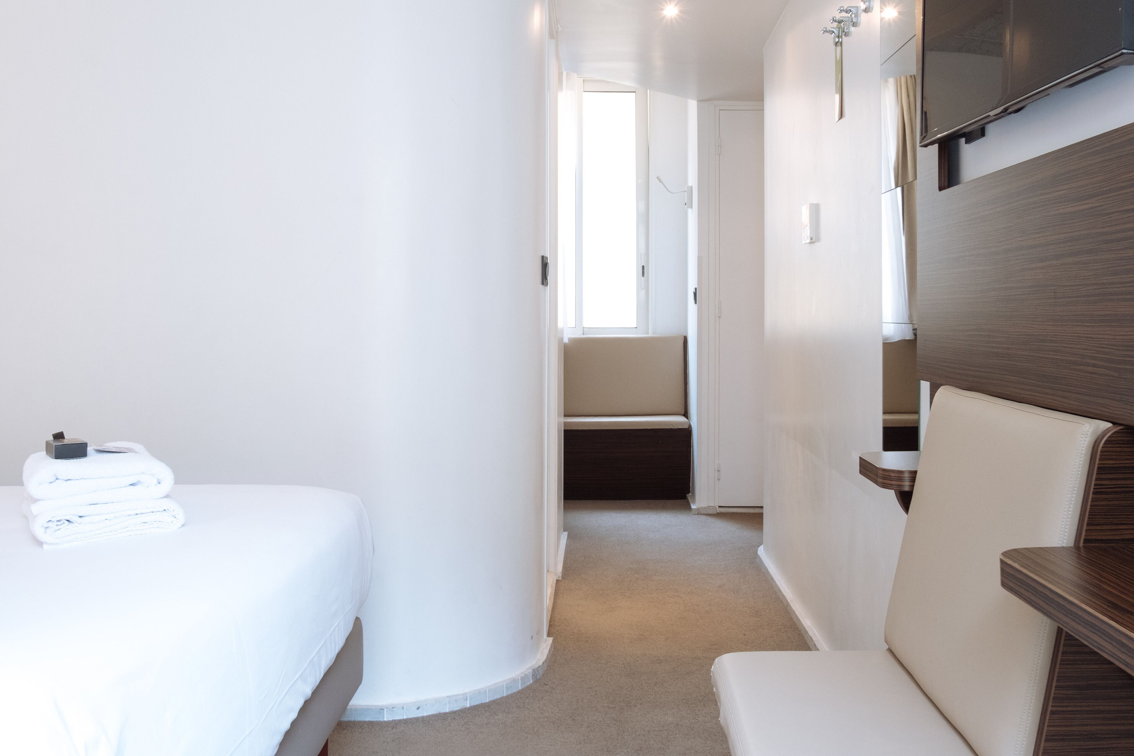 A compact, modern room with a bed, a seating area, and a TV mounted on the wall.