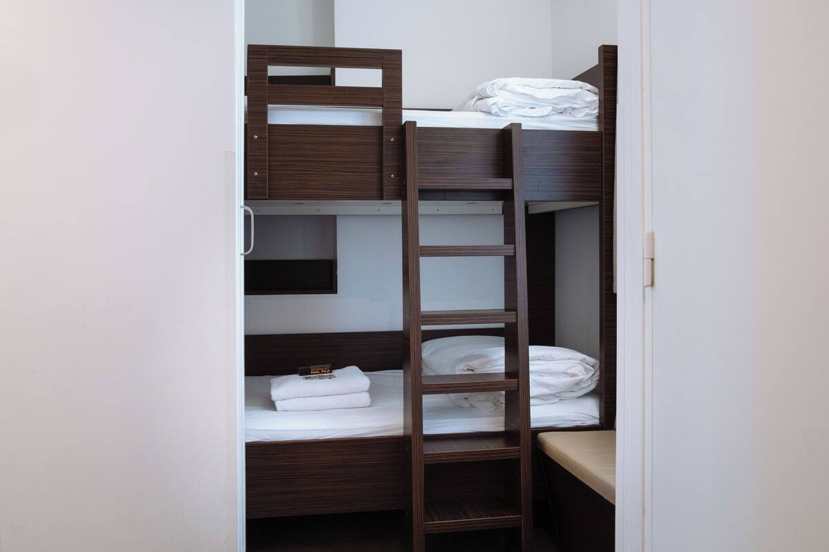 A bunk bed with a ladder, a small shelf, and a white towel on the lower bunk.