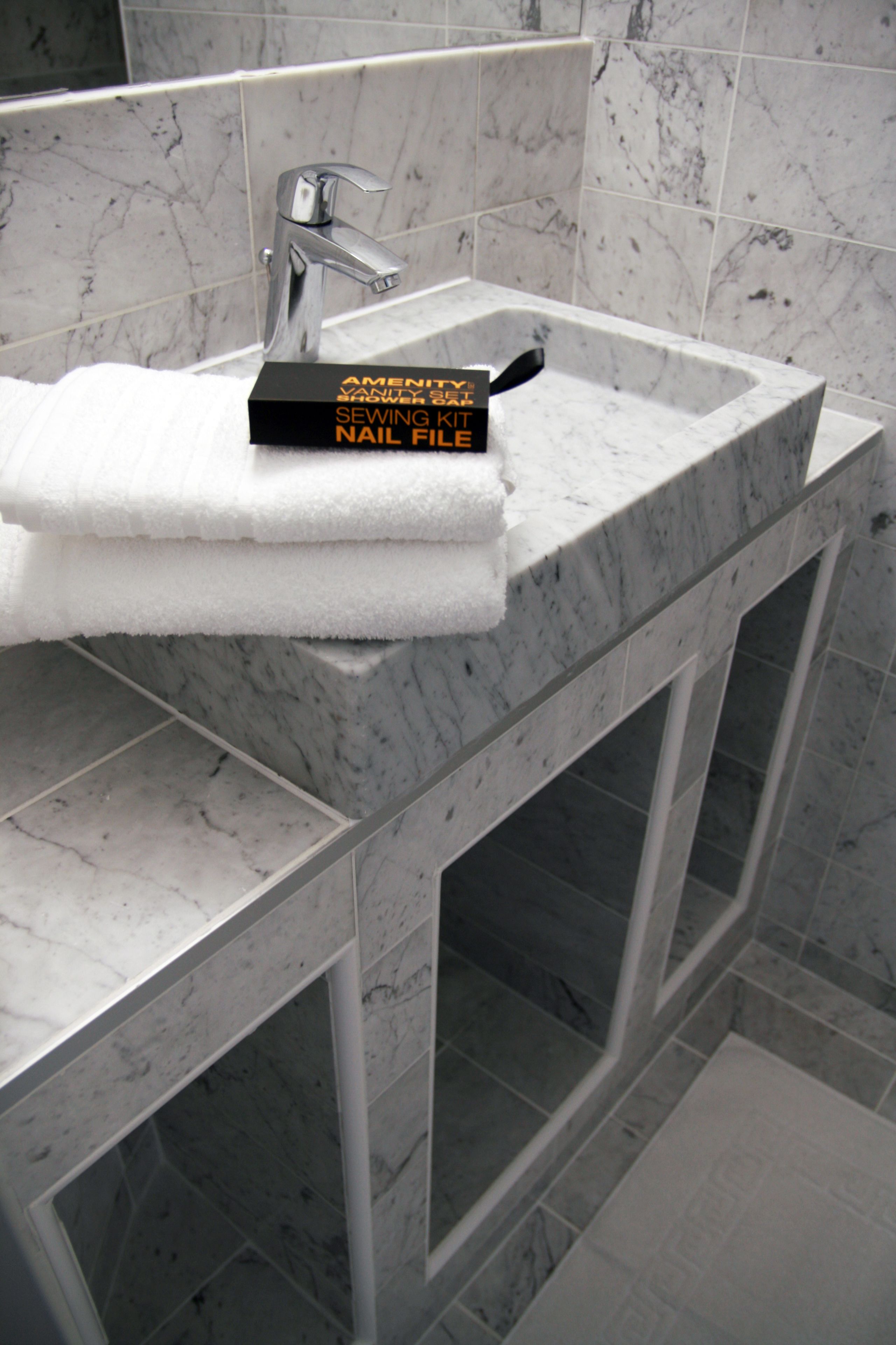 A bathroom with a marble sink, a towel, and a book titled "SEWING KIT NAIL FILE".