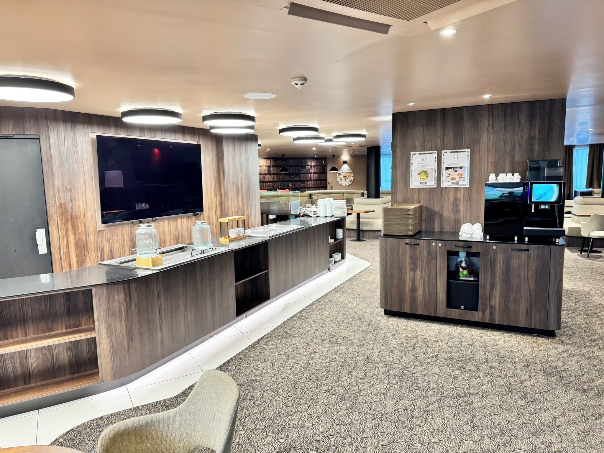 En moderne hotellobby med reception, fladskærm, kaffemaskine og en reol.