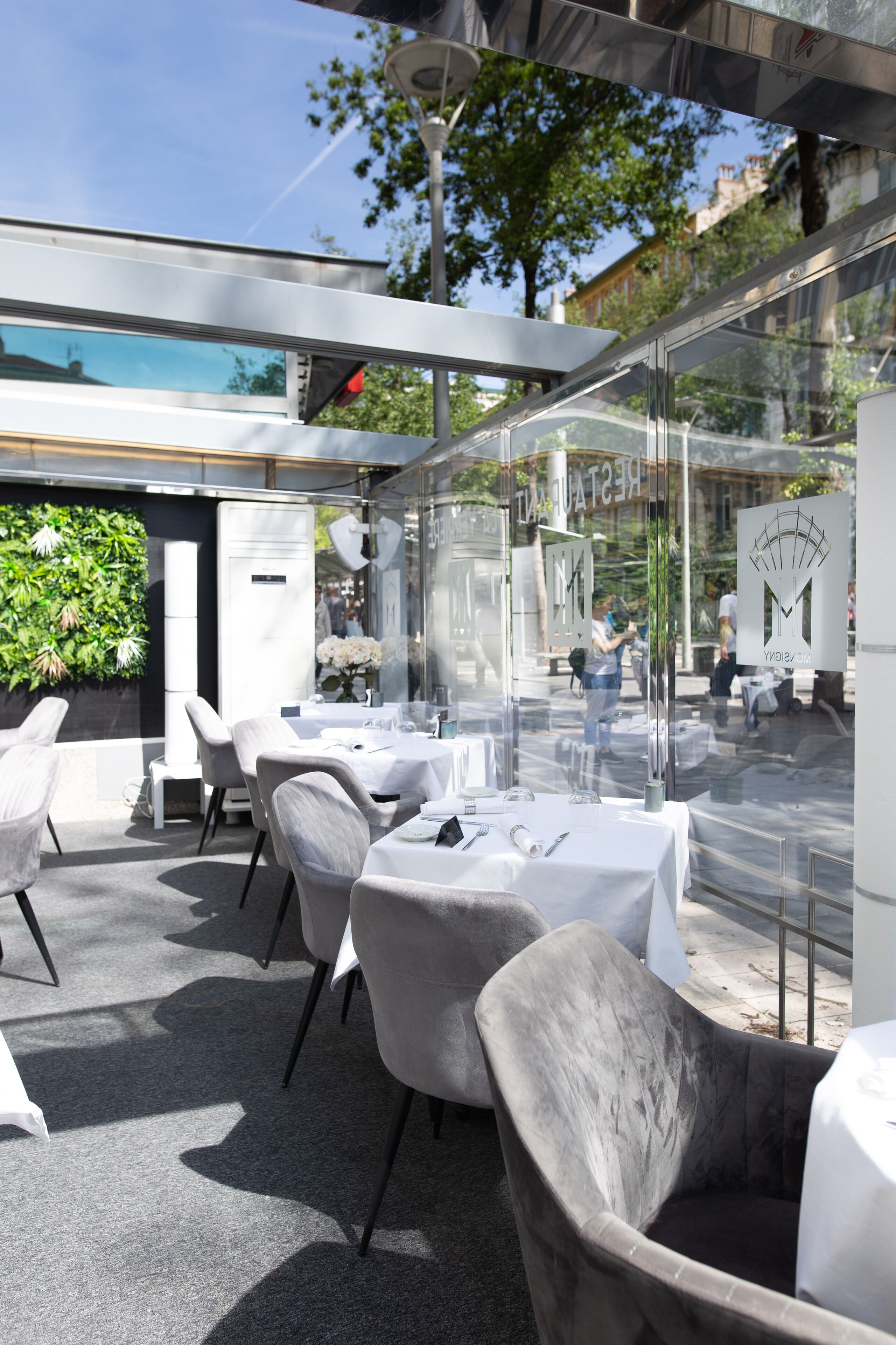 Un espace de restauration en plein air avec des tables et des chaises, un mur en verre et une vue sur la rue.
