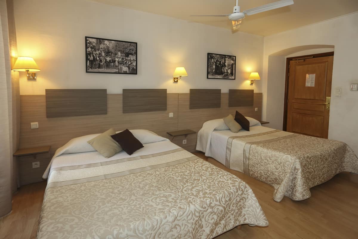 A hotel room with two beds, each with a headboard, bedside lamps, and framed pictures on the wall.
