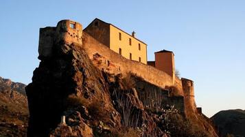 A historic stone building perched on a rocky cliff with a small tower and a separate building attached to the main structure.