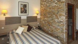 Une chambre d’hôtel avec un lit, deux lampes fixées au mur, un tableau encadré et un mur décoratif en pierre.