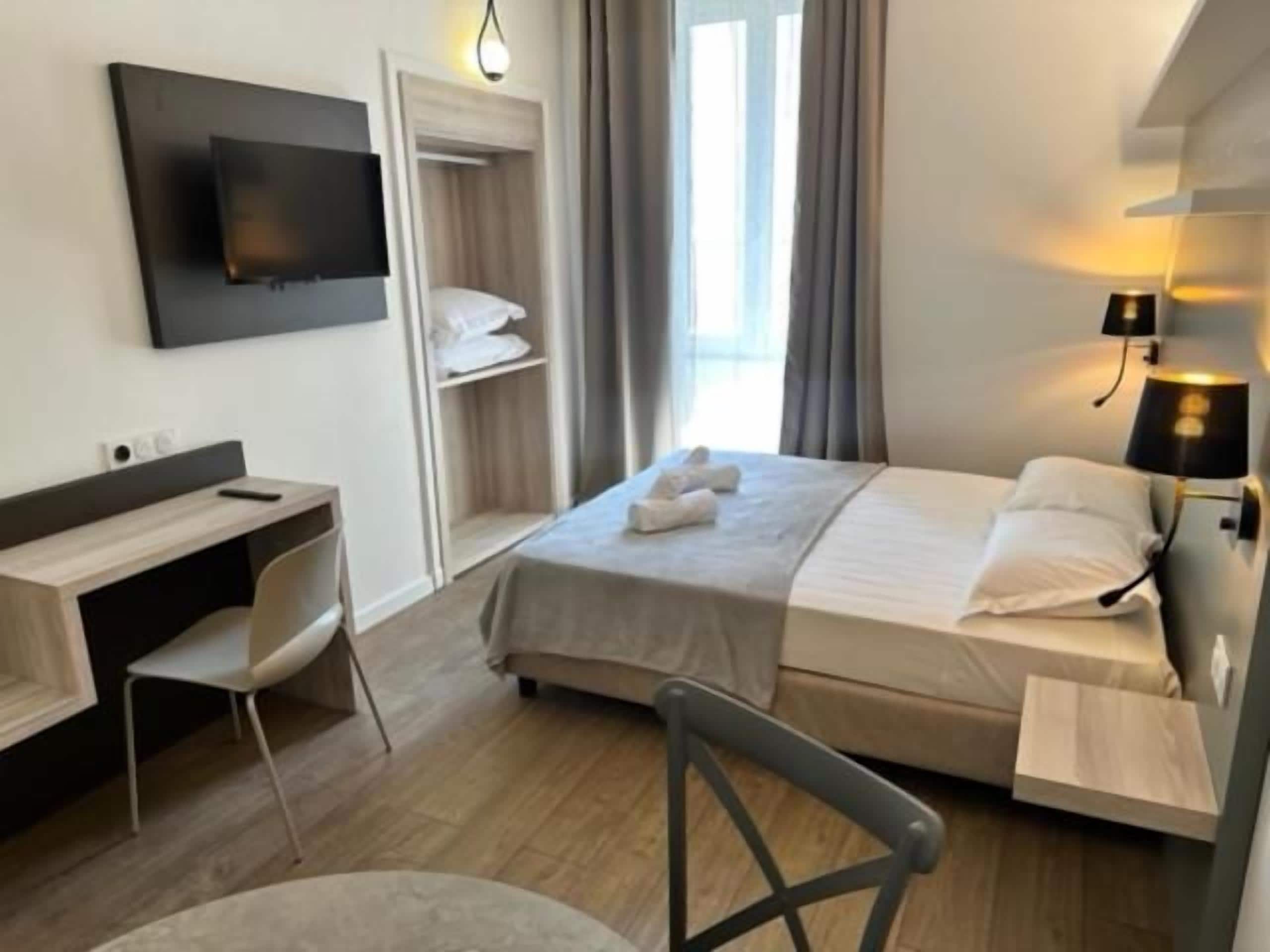 Habitación de hotel con cama, escritorio, silla, televisor y mesita de noche.
