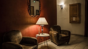 Une pièce comprenant deux fauteuils en cuir, une petite table ronde avec une lampe, un miroir et un luminaire fixé au mur.