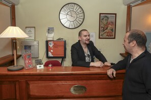 A reception desk with a clock, framed certificates, and a poster on the wall.