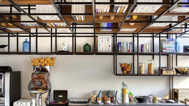 Una cocina moderna con cafetera, una cesta de fruta y varios libros en estanterías.