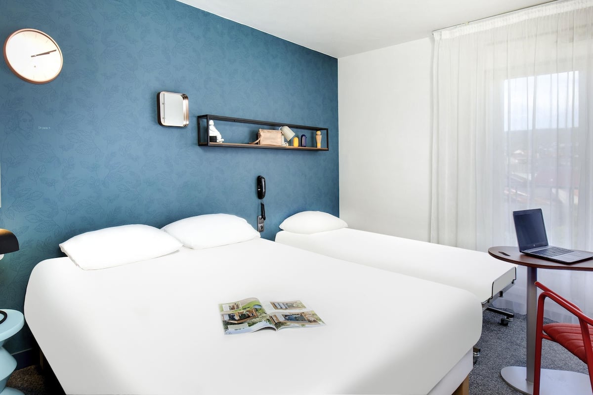 Una habitación de hotel con una cama grande, un escritorio con una computadora portátil, un teléfono, un reloj y una ventana con cortinas.