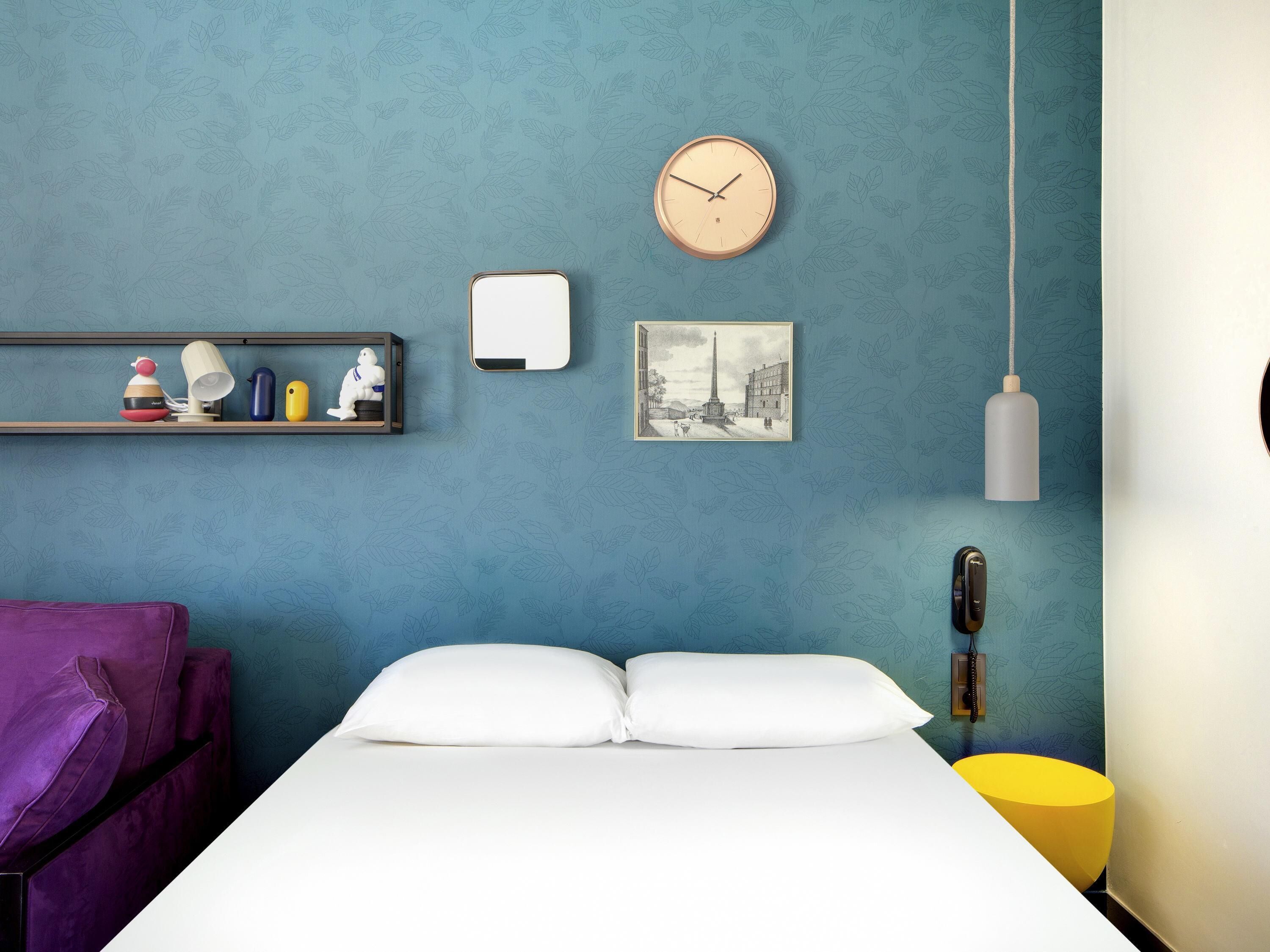 A room with a bed, a clock, a shelf with decorative items, a picture, and a hanging light fixture.