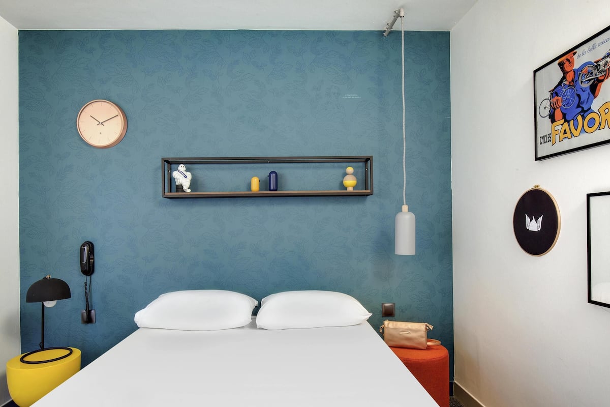 Un dormitorio con cama, un reloj, una estantería con adornos, una lámpara colgante y un cuadro en la pared.