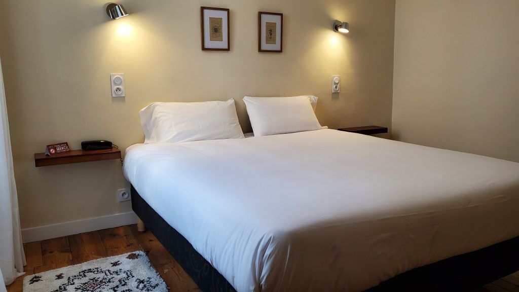 Un lit bien fait, avec du linge de lit blanc, une tête de lit en bois et deux tables de chevet avec des lampes.