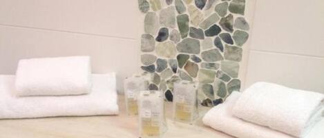 Une salle de bain avec un mur décoré d’une mosaïque en pierre, un meuble-lavabo blanc et deux serviettes blanches.