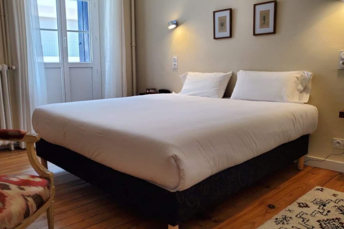 Habitación de hotel con una cama grande, una silla, un radiador y una ventana.