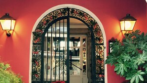 Ein Hotelzugang mit roter Wand, einem schwarzen schmiedeeisernen Tor und zwei Wandleuchten.