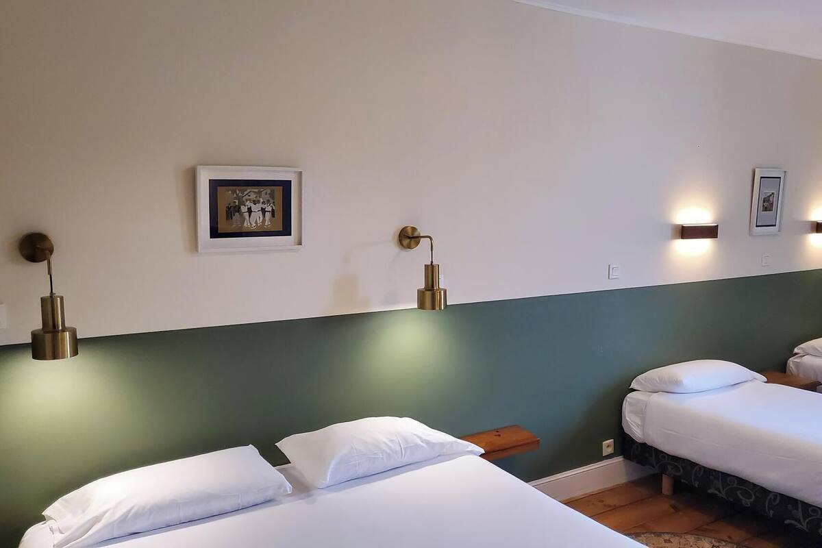 Habitación de hotel con dos camas individuales, un cuadro en la pared y dos luces fijadas a la pared.