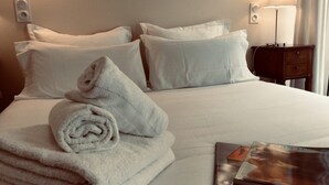 Ein ordentlich bezogenes Bett mit weißen Leinen, ein zusammengerolltes Handtuch und ein kleiner Nachttisch mit einer Lampe.