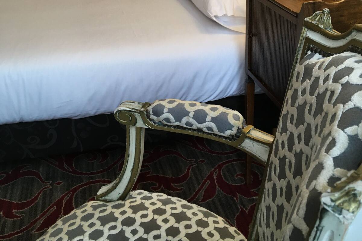 Una habitación de hotel con dos camas, una silla, una lámpara y una mesita de noche.