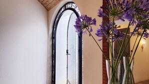 Ein Flur mit Ziegeldecke, einer weißen Tür mit schwarzem Metallrahmen und einer Vase mit violetten Blumen auf einem Tisch.