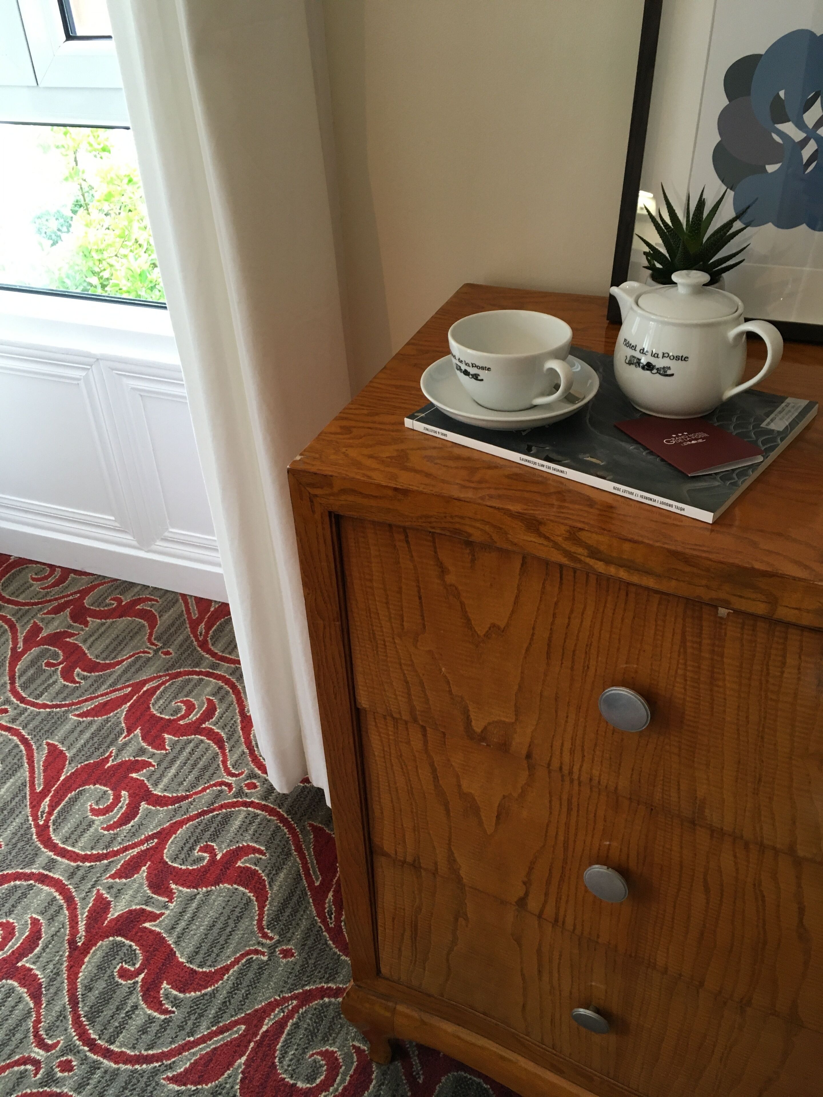 A wooden cabinet with a white teapot and cups on top, a patterned rug, and a door with a white frame.