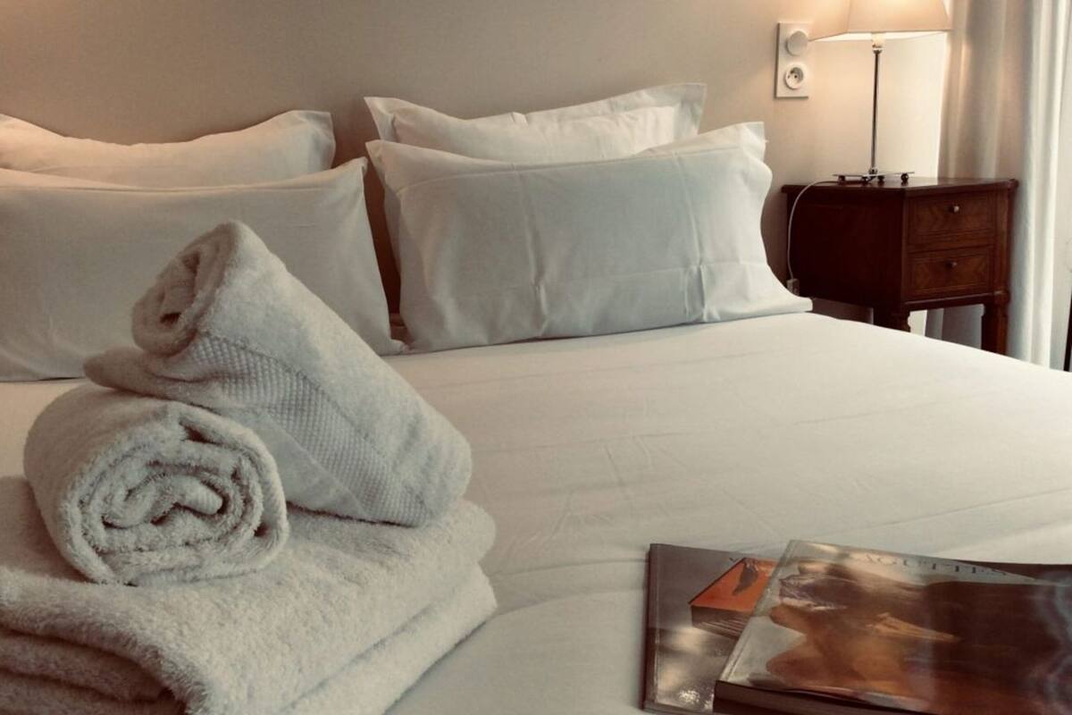 Una cama bien hecha con sábanas blancas, una toalla enrollada y una revista al lado.