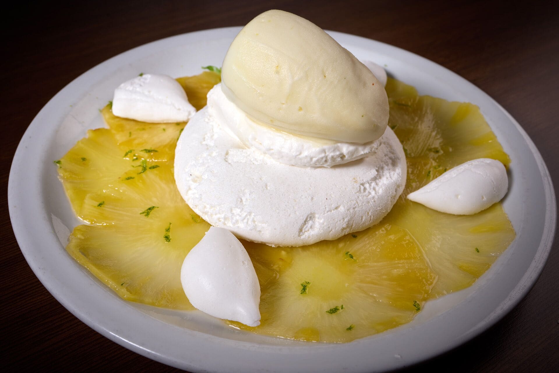 Un plato con un postre blanco sobre una base amarilla, posiblemente un plato a base de frutas, adornado con hierbas.