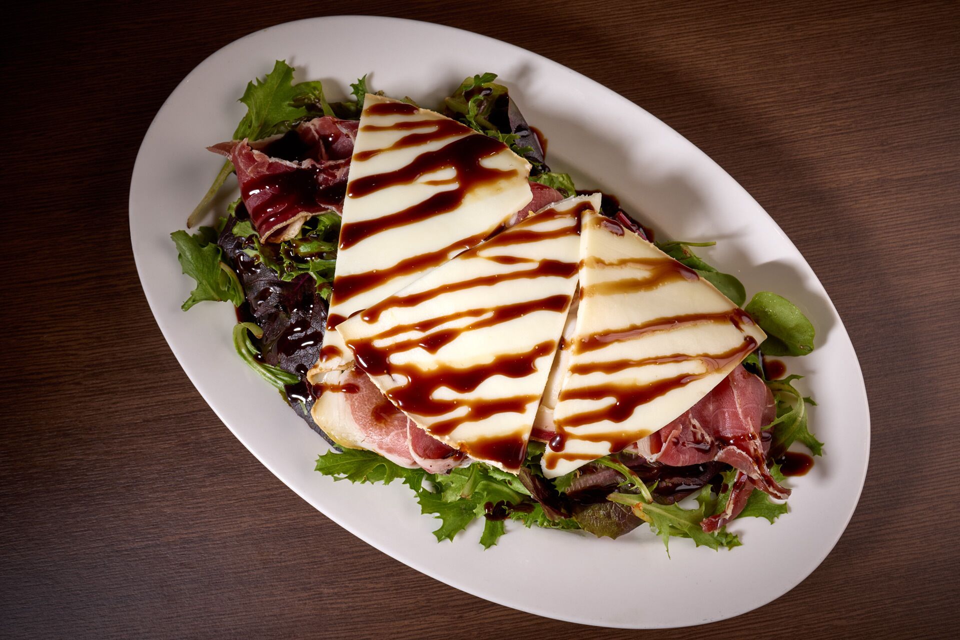 A plate with a sandwich, salad, and a drizzle of sauce.