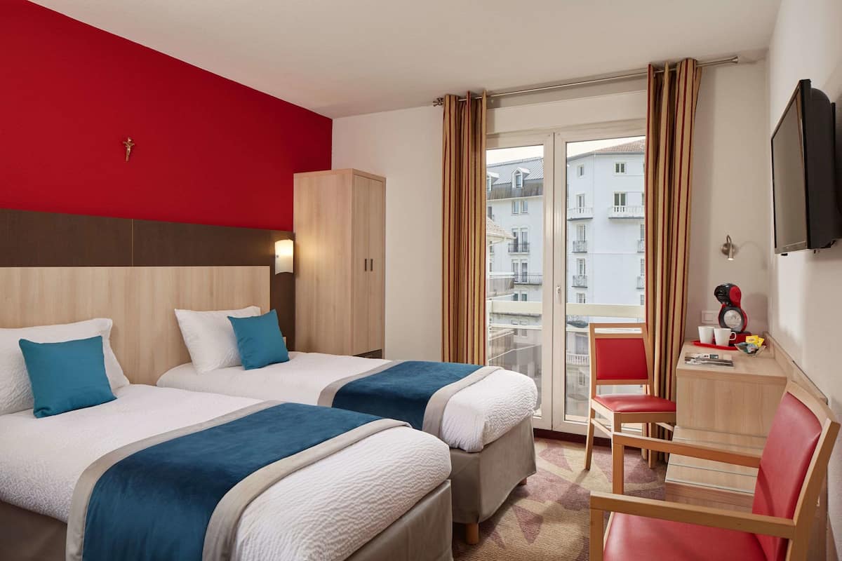 A hotel room with two beds, a desk, a chair, and a TV.