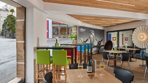 A modern cafe with wooden ceiling, colorful chairs, and a wine bottle on the table. - Hotel Roissy Lourdes (Lourdes)