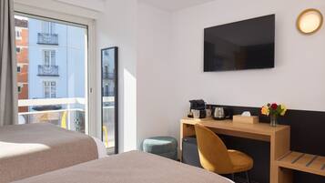 A hotel room with two beds, a desk with a chair, a television, and a window with a view of buildings.