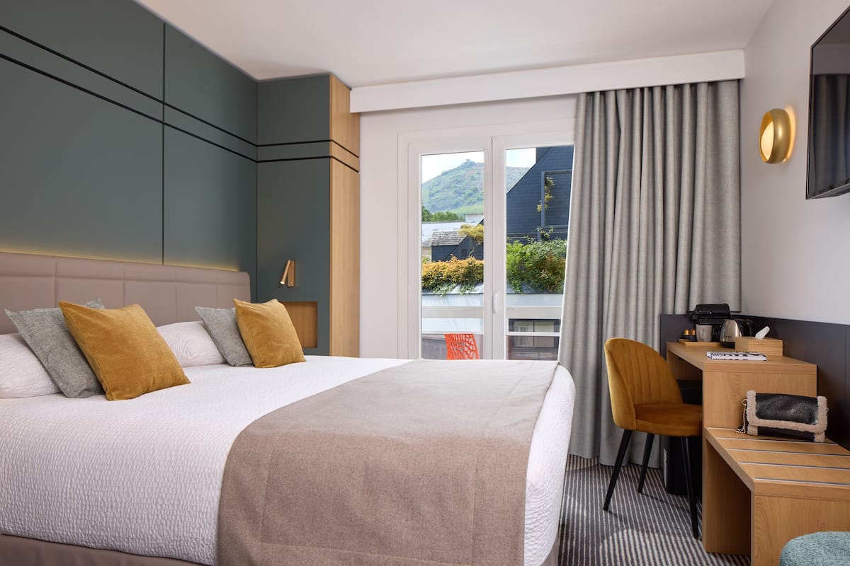 A hotel room with a large bed, a desk, a chair, and a view of the outdoors.