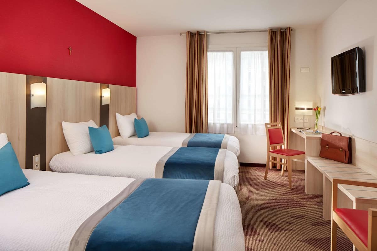 A hotel room with three beds, a desk, a chair, and a TV.