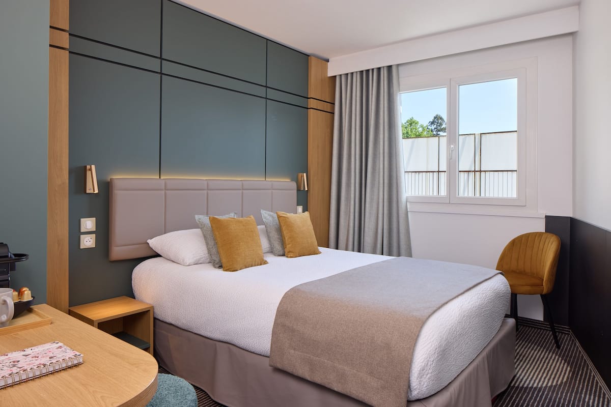 A hotel room with a bed, bedside table, chair, and a window with curtains.