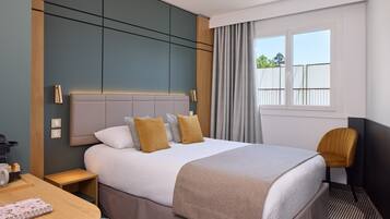 A hotel room with a bed, bedside table, chair, and a window with curtains.