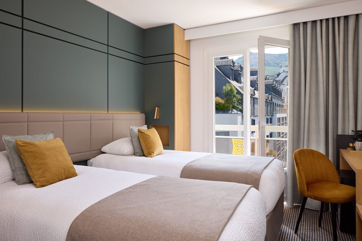 A hotel room with two beds, a desk, a chair, and a view of the city.
