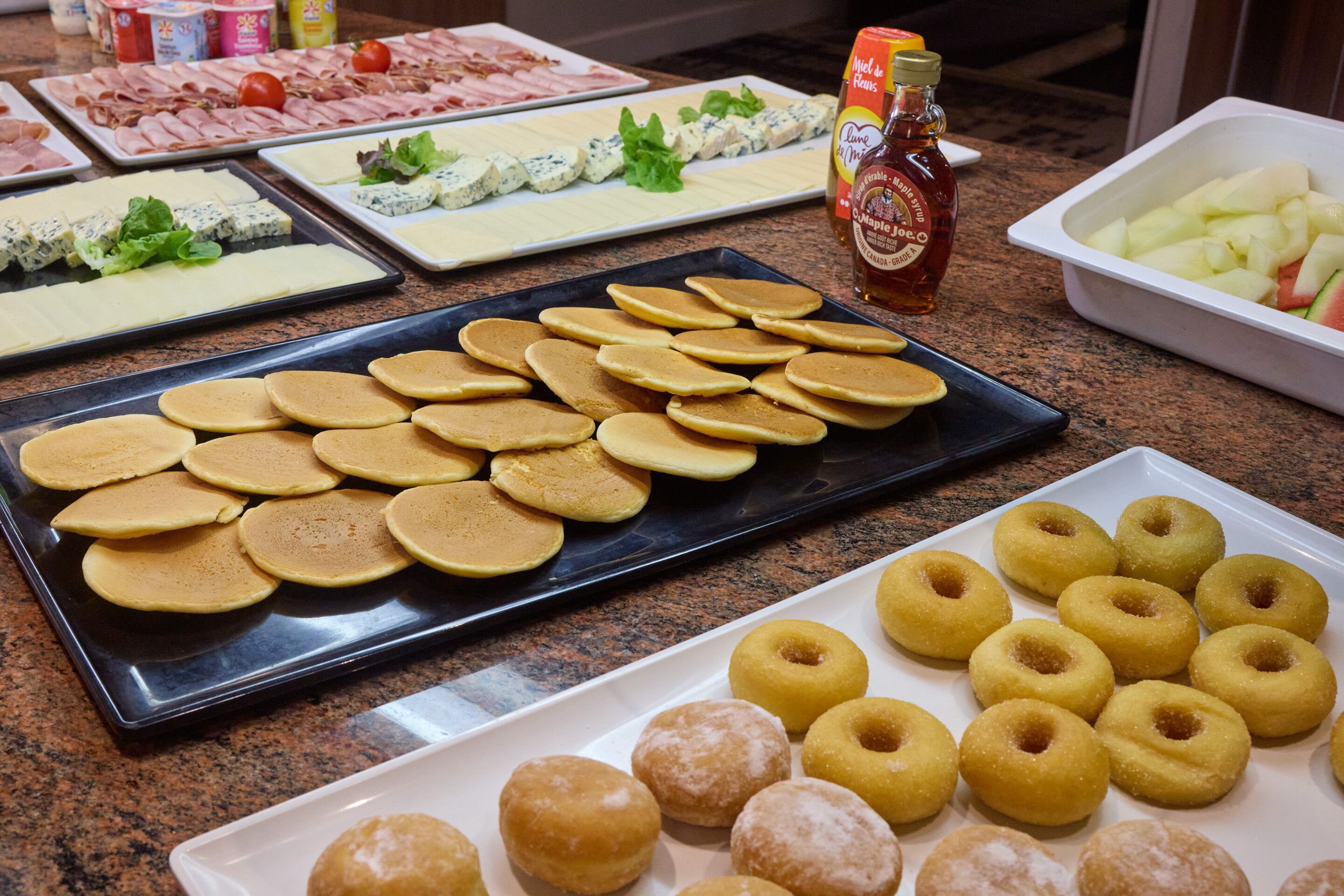 A buffet with various food items including pancakes, donuts, and cheese.
