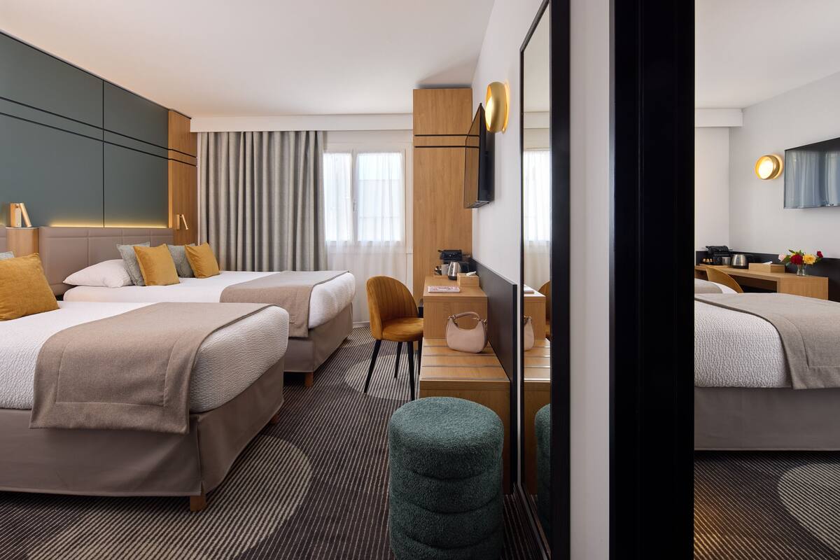 A hotel room with two beds, a desk, a chair, a mirror, and a large window with curtains.
