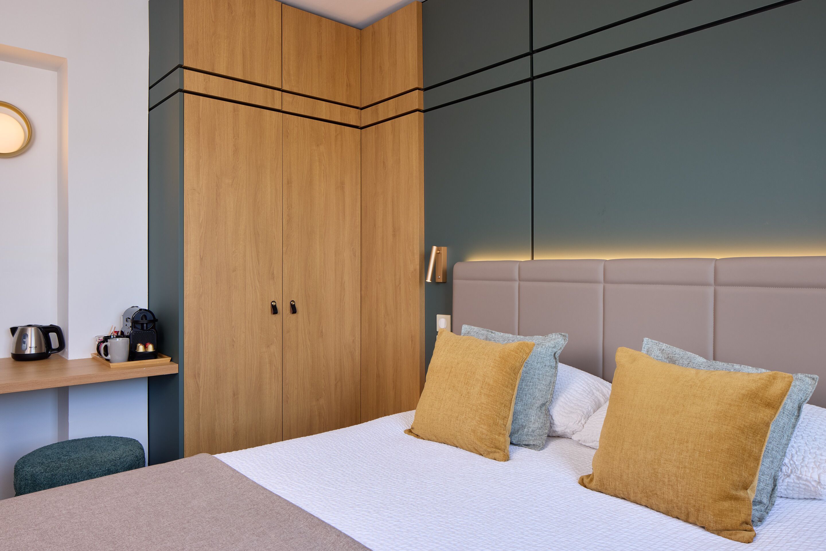 Un dormitorio moderno con cama, un armario de madera, una mesita de noche con tetera y una mesita auxiliar.