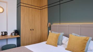 Un dormitorio moderno con cama, un armario de madera, una mesita de noche con tetera y una mesita auxiliar.