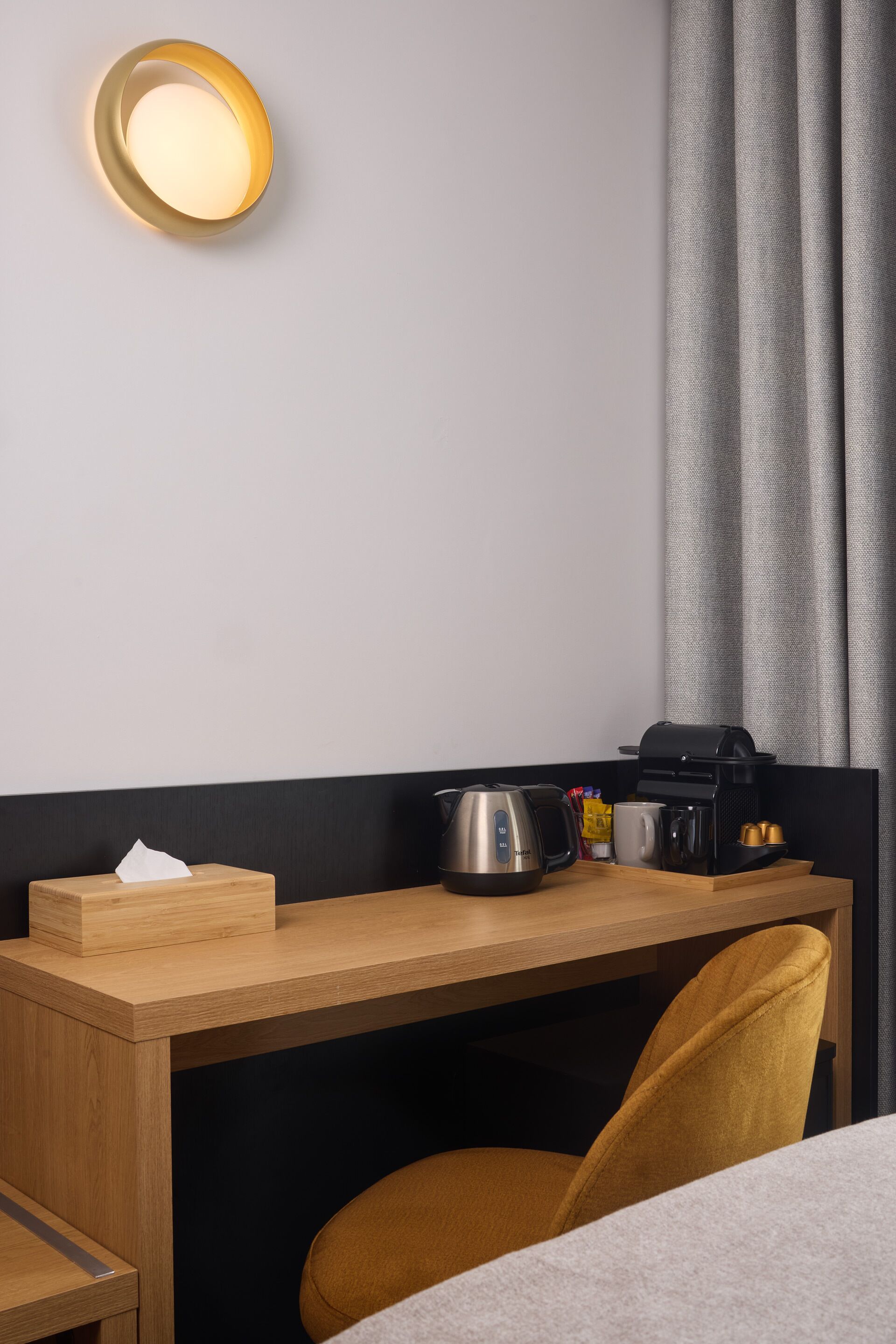 A hotel room with a wooden desk, a coffee maker, a kettle, and a tissue box.