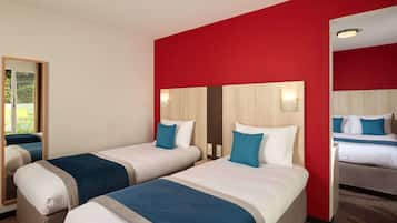 Habitación de hotel con dos camas, una pared de acento roja y un espejo que refleja la habitación.