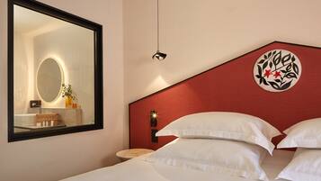 Une chambre d’hôtel avec un grand miroir, un lit recouvert de draps blancs, un mur d’accent rouge et un élément décoratif mural.