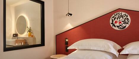 Une chambre d’hôtel avec un grand miroir, un lit recouvert de draps blancs, un mur d’accent rouge et un élément décoratif mural.