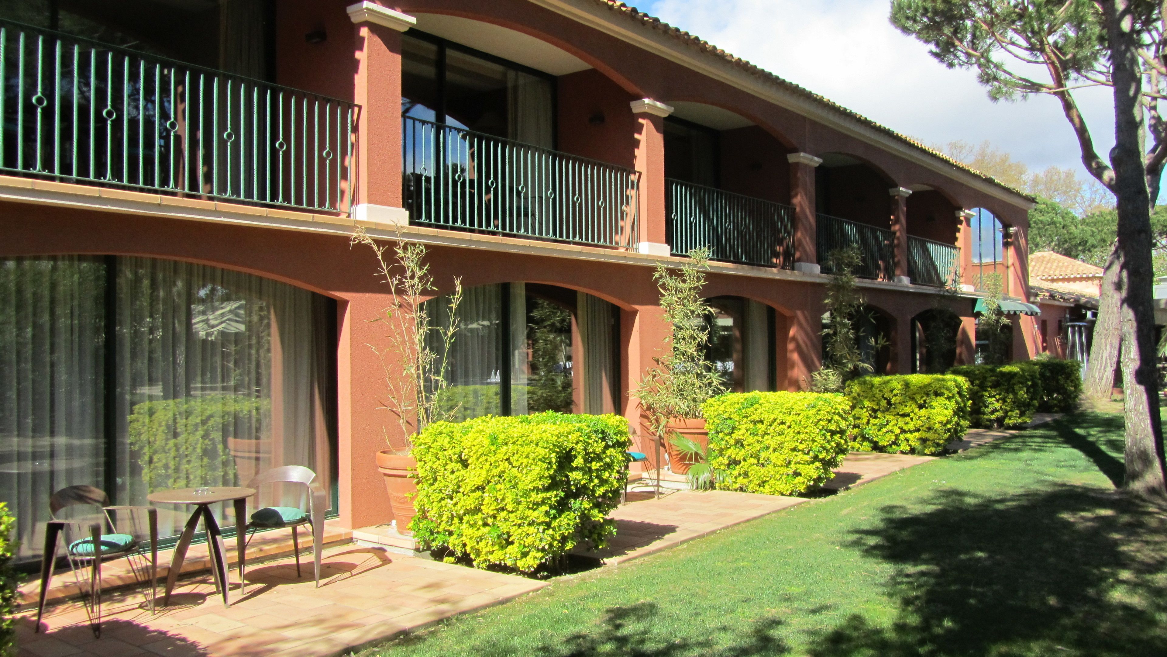 A hotel with a red facade, multiple balconies, and a well-maintained lawn.
