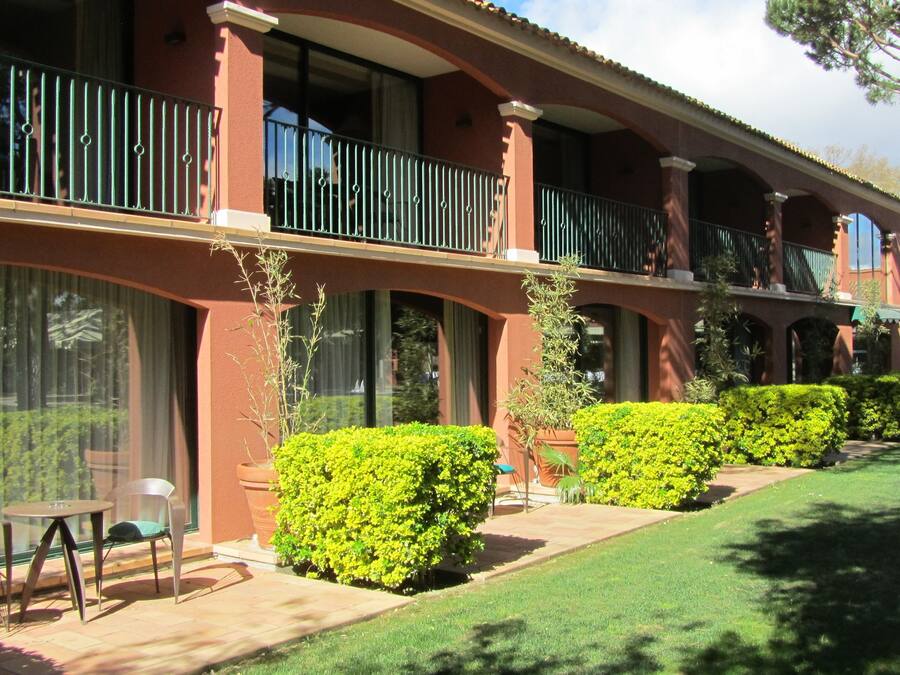 A hotel with a red facade, multiple balconies, and a well-maintained lawn.