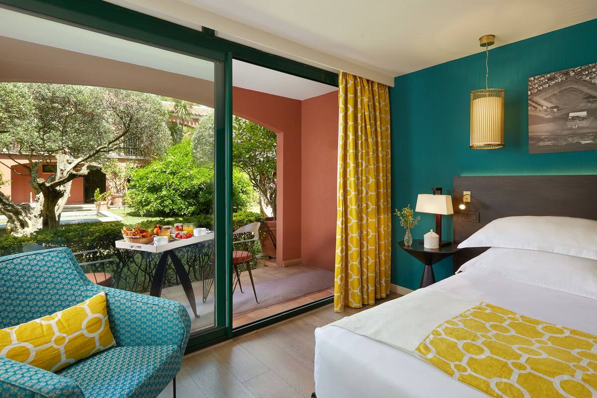 A hotel room with a bed, a sofa, a table with breakfast items, and a view of the outside.