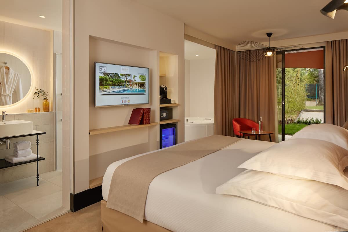 A modern hotel room with a large bed, a TV mounted on the wall, a red chair, and a view of the outdoors.