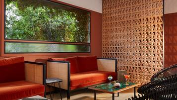 Una habitación moderna con un ventanal grande, un sofá rojo, un sillón de mimbre, una mesita con una bebida y una pared con diseño.